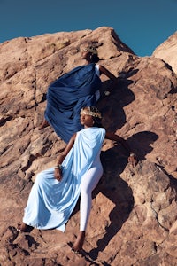 two women sitting on top of a rock in a blue dress