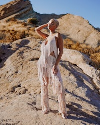 a woman in a fringed dress standing on a rock