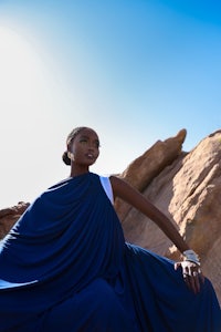 a woman in a blue dress sitting on a rock